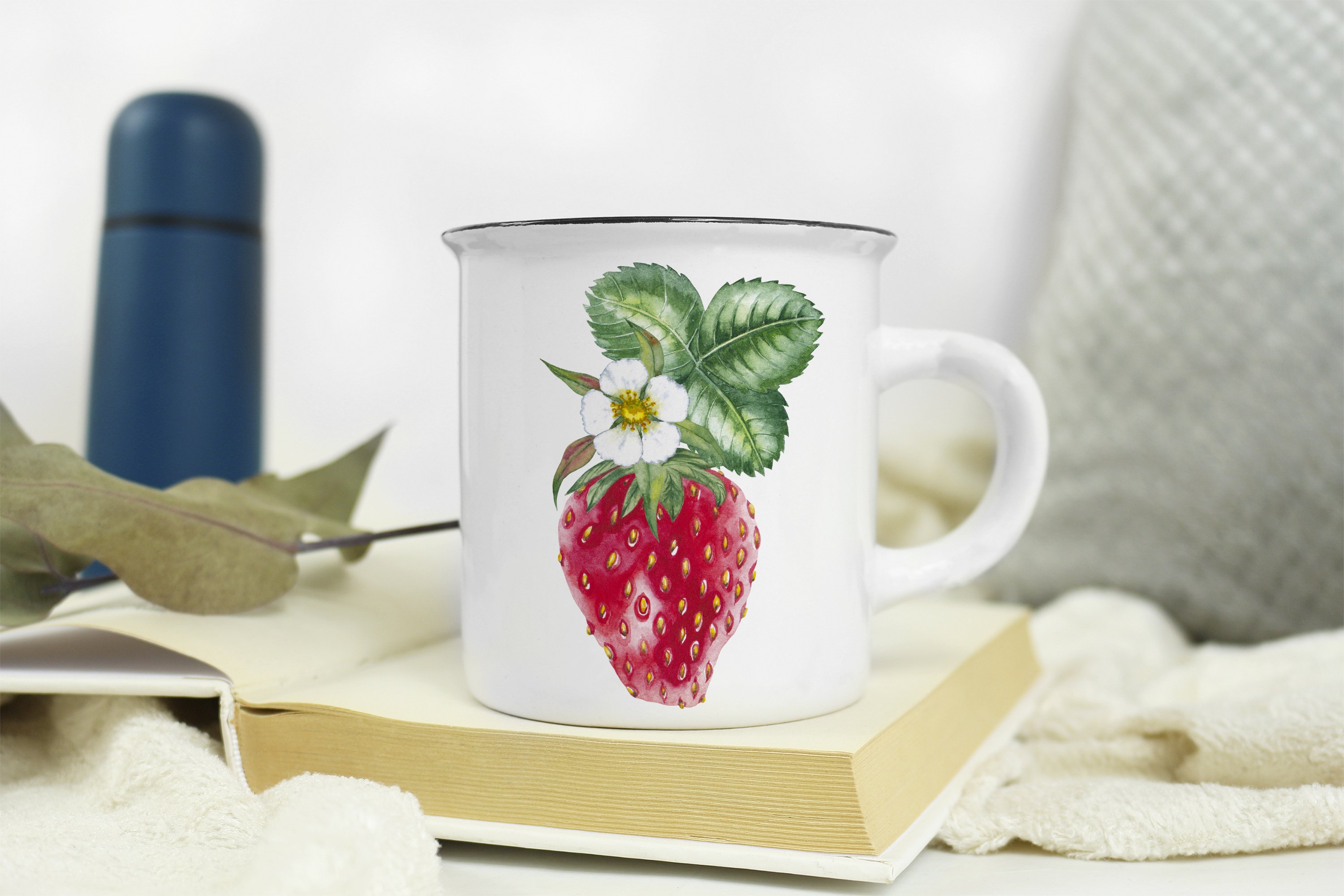 White cup on a book with illustration of a strawberry.