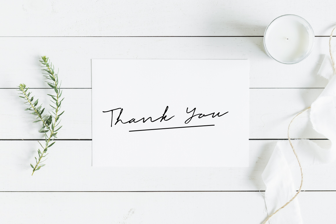 Black script lettering "Thank you" on a white sheet on the table.