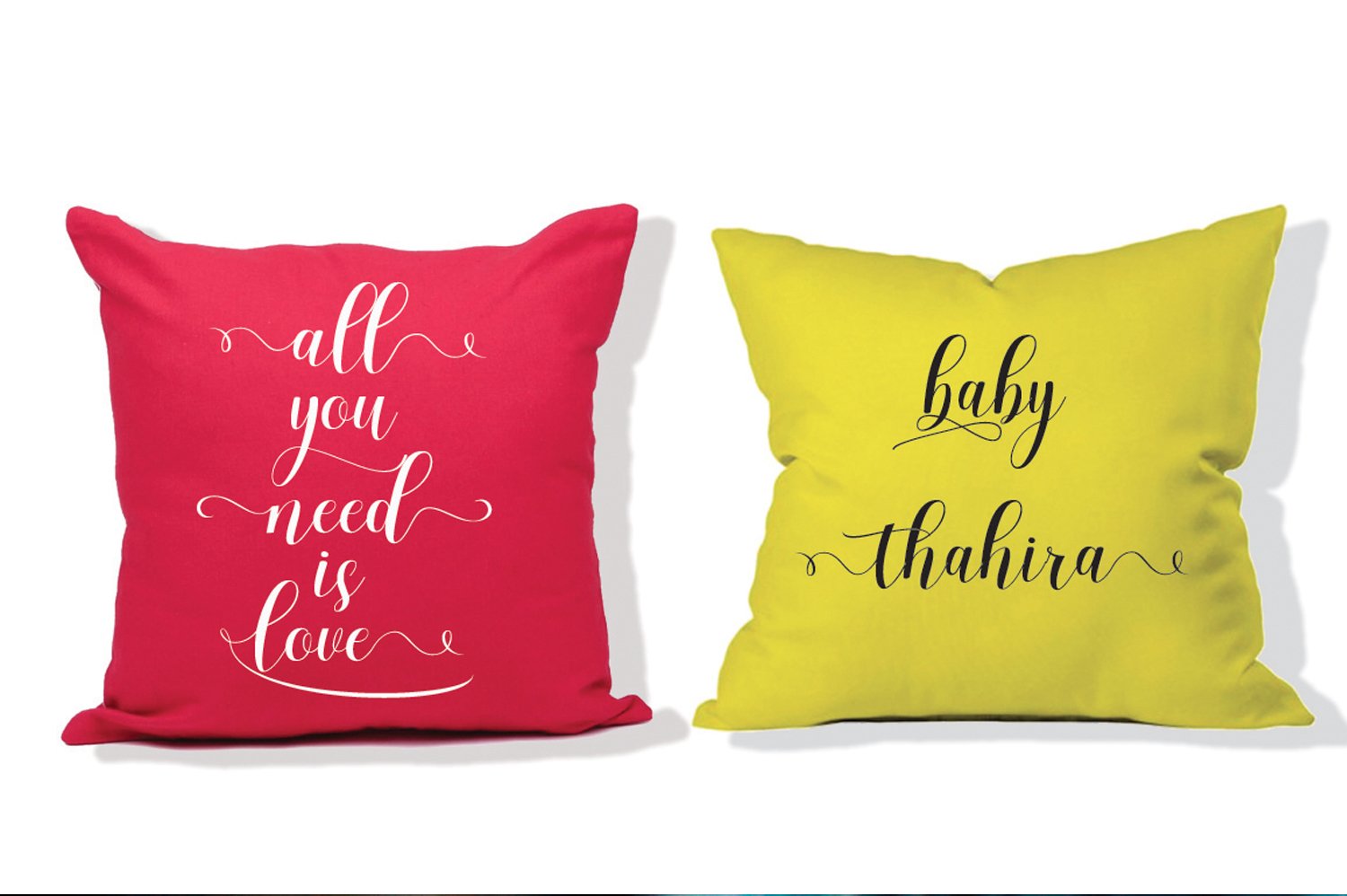 Pink and dirty yellow pillows with white and black lettering on a white background.