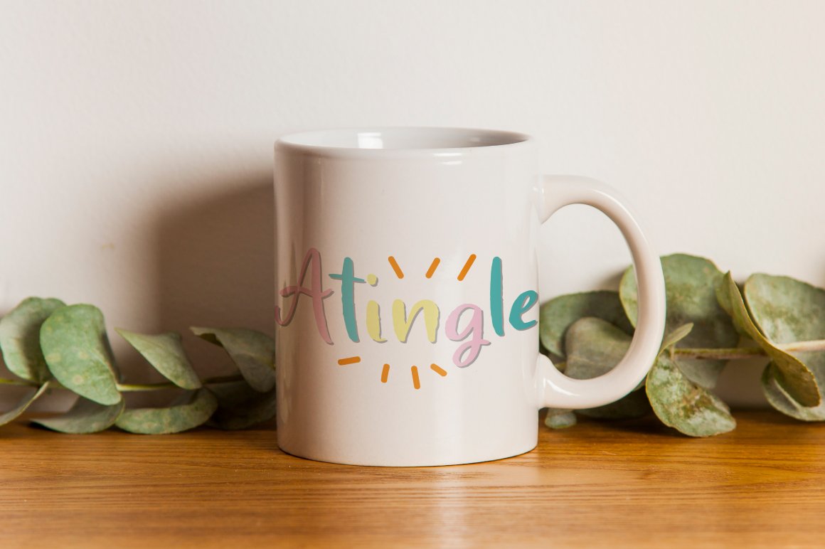 Cup with colorful calligraphy lettering "Atingle" on the table.