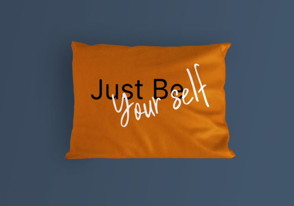 Orange pillow with black and white lettering "Just Be Your Self" on a blue background.