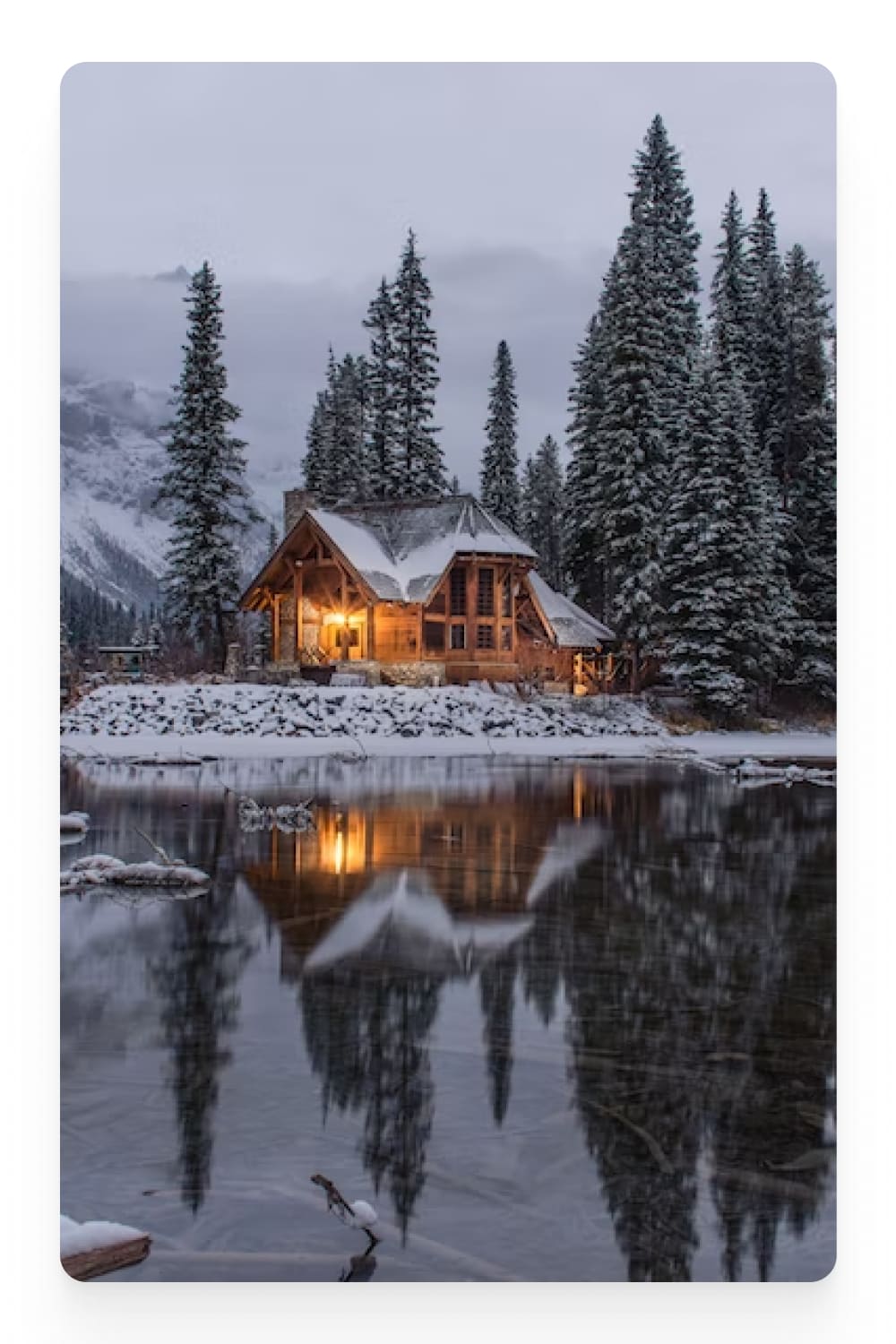 Photo of a house by the lake and firs covered with snow.