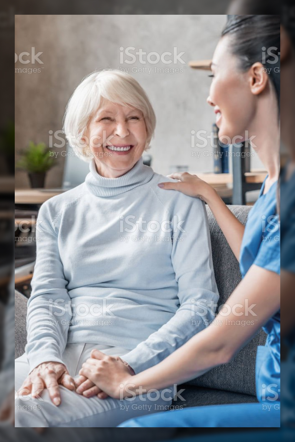 Vertical shot of helpful nurse taking care of senior woman in nursing home stock photo.