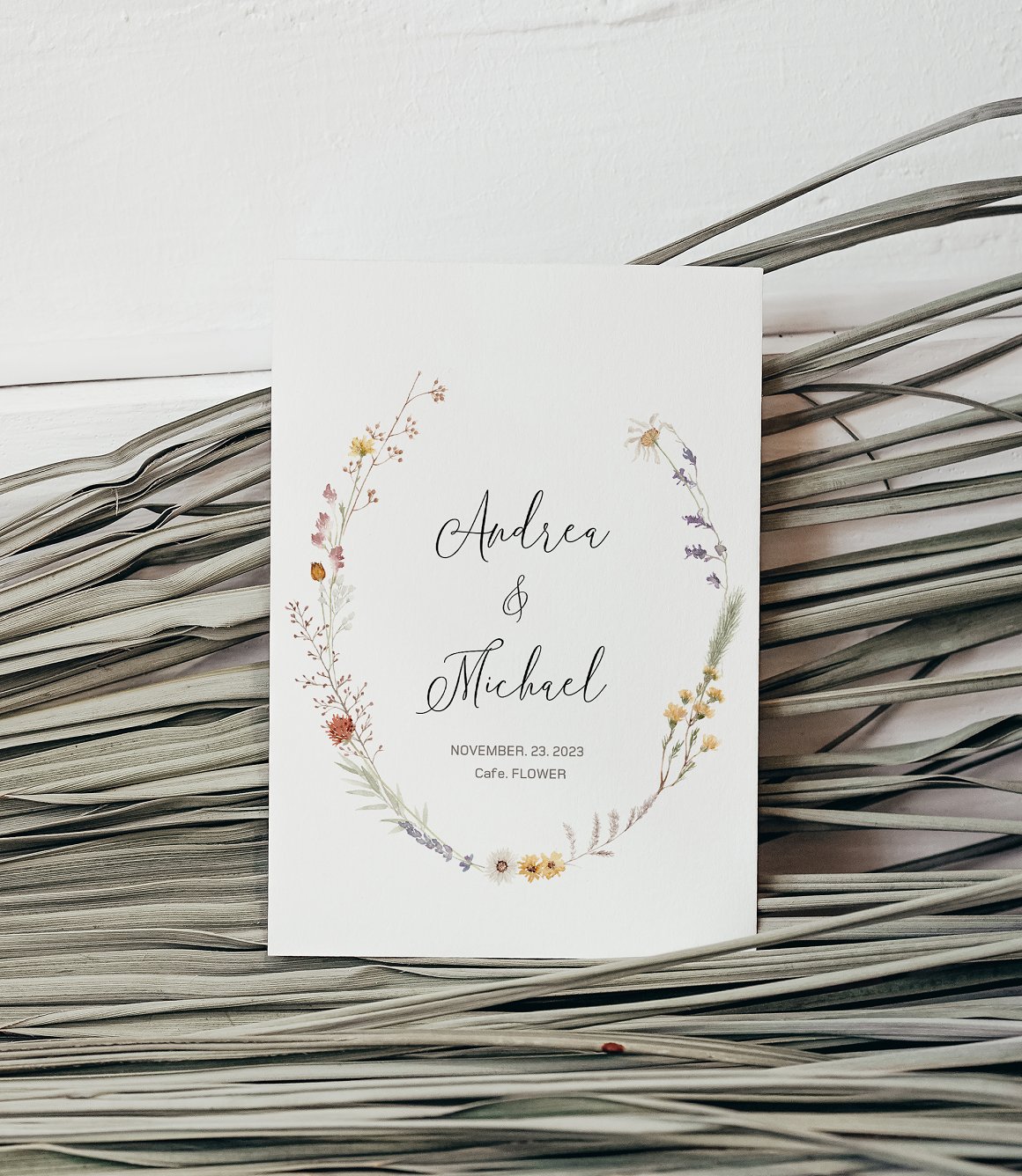 White vertical wedding card with black lettering and floral wreath.