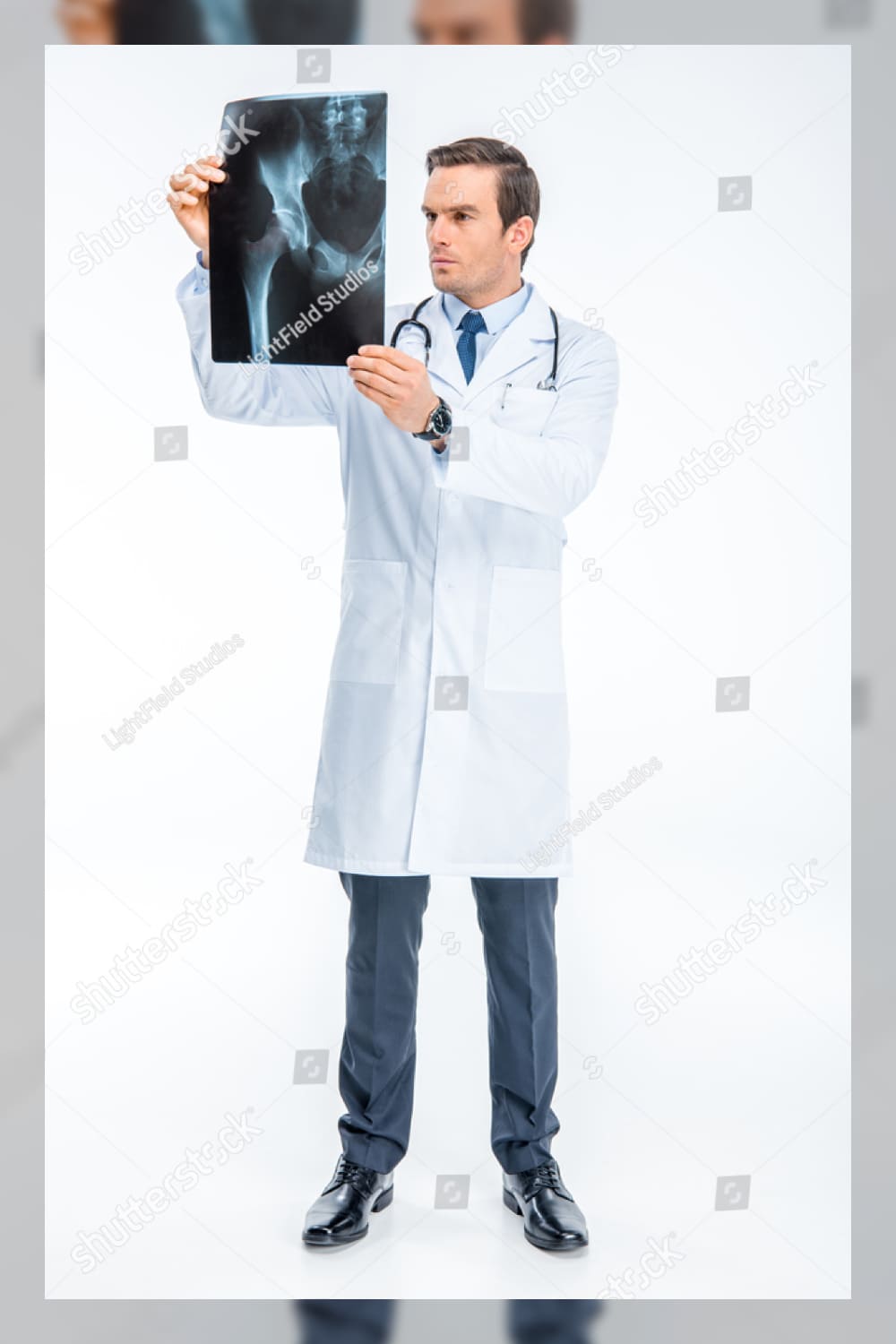 Full length portrait of handsome male doctor looking at x ray image isolated on white.