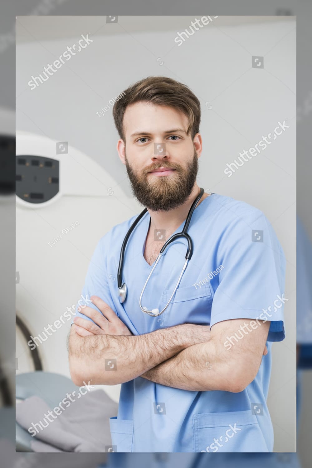 Male doctor standing arms crossed in examination room.