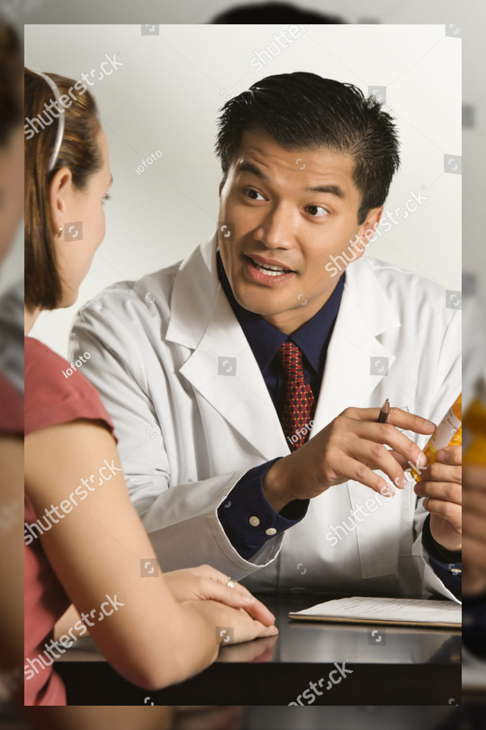 Asian american male doctor explaining medication to caucasian female patient.