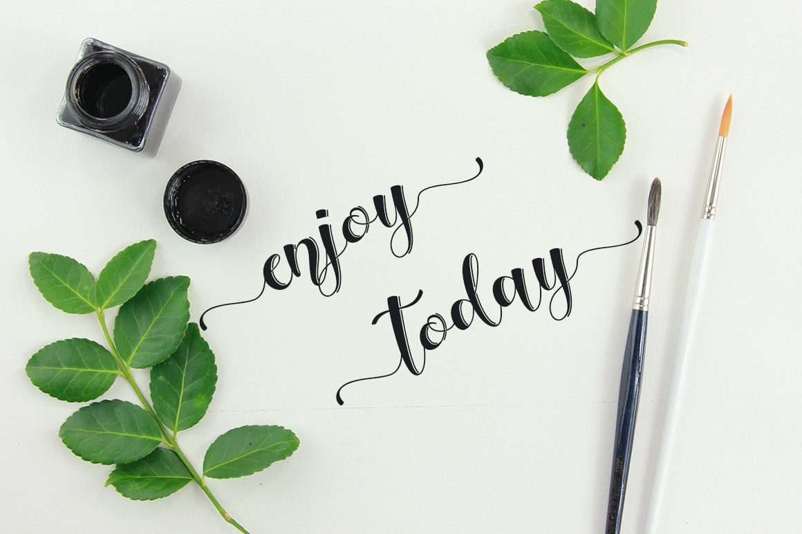 Black "Enjoy today" calligraphy lettering on a gray background with leaves.
