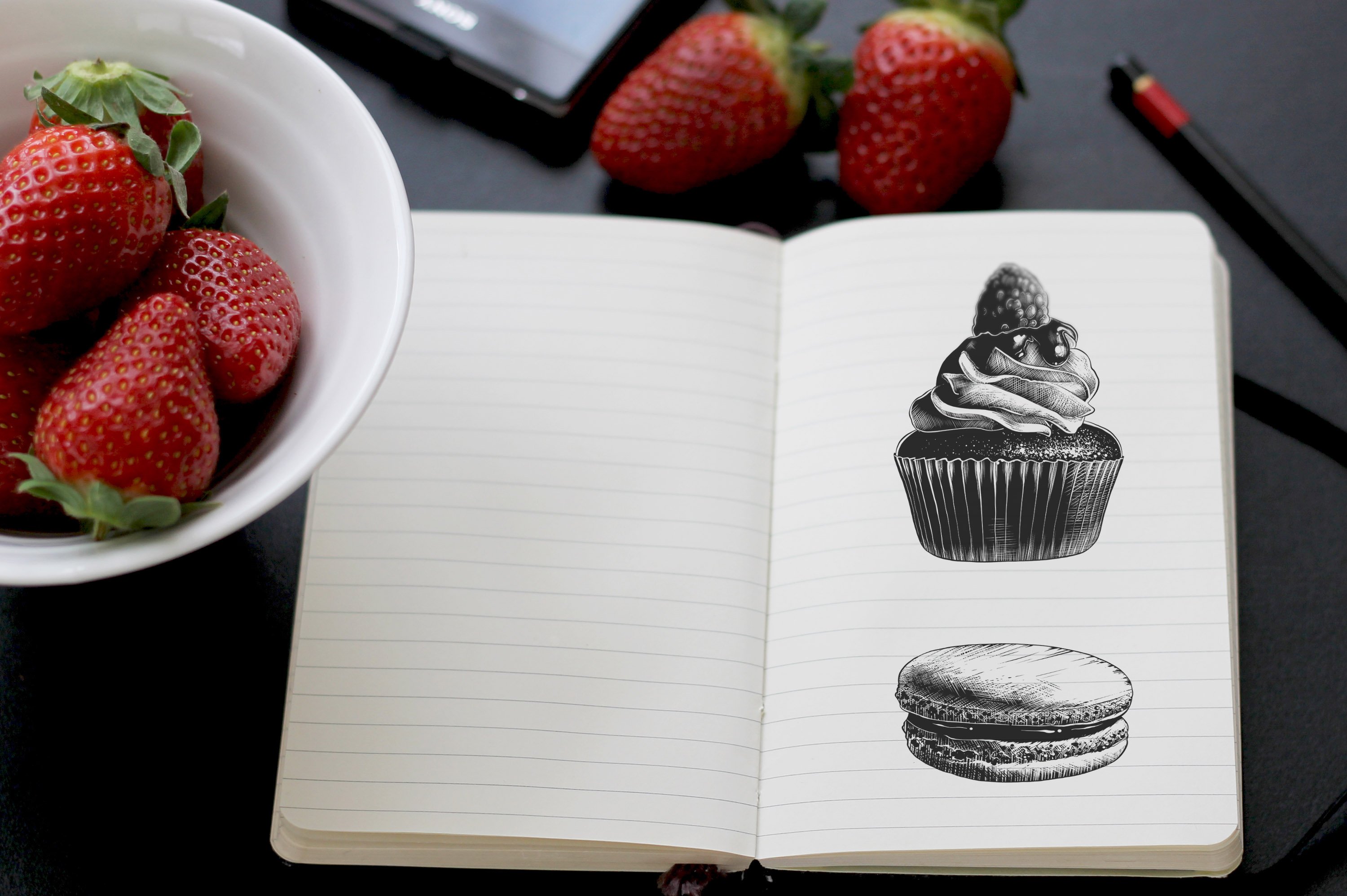 A notebook with a drawing of a cupcake and a bowl of strawberries.