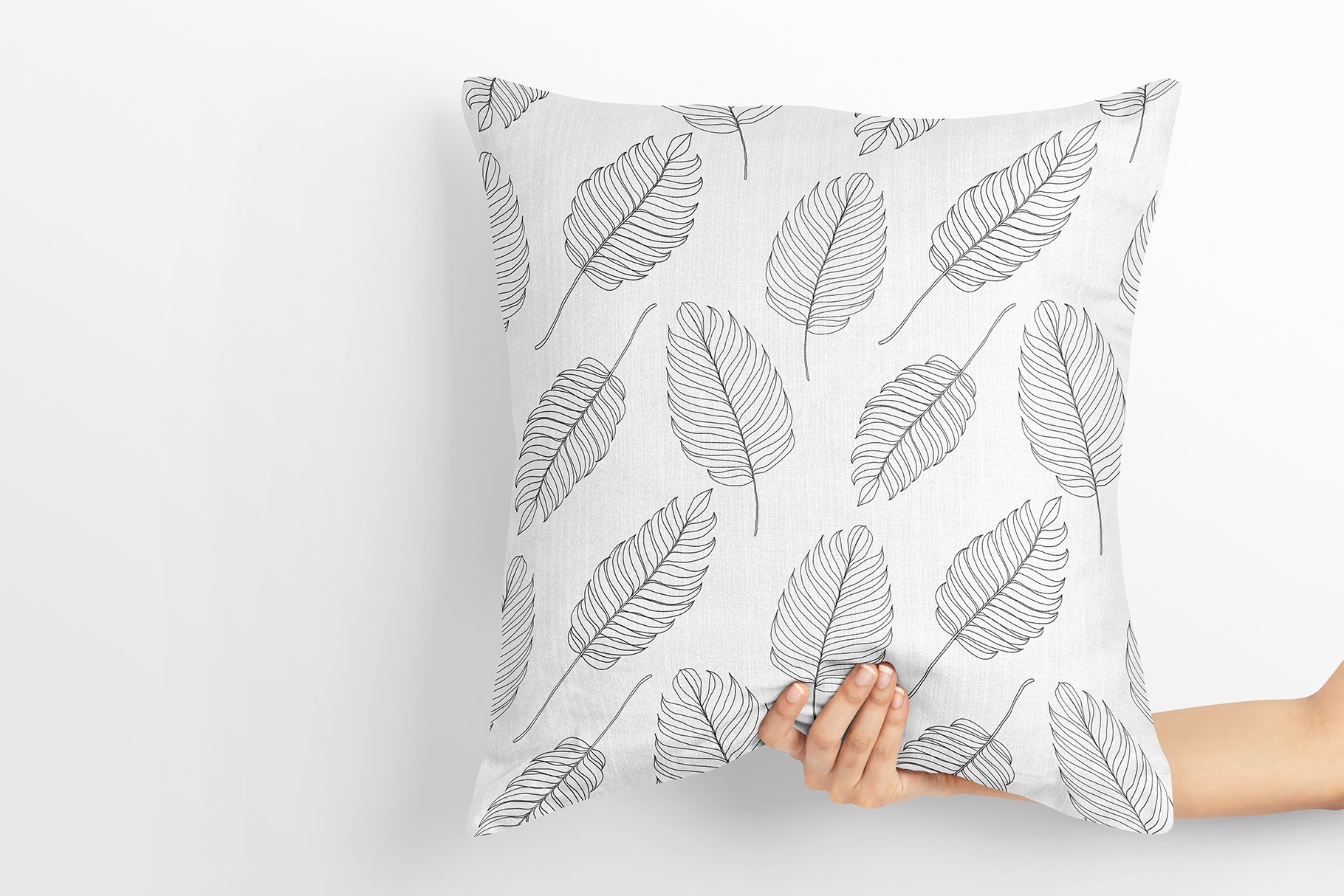 Person holding a pillow with a pattern of leaves on it.