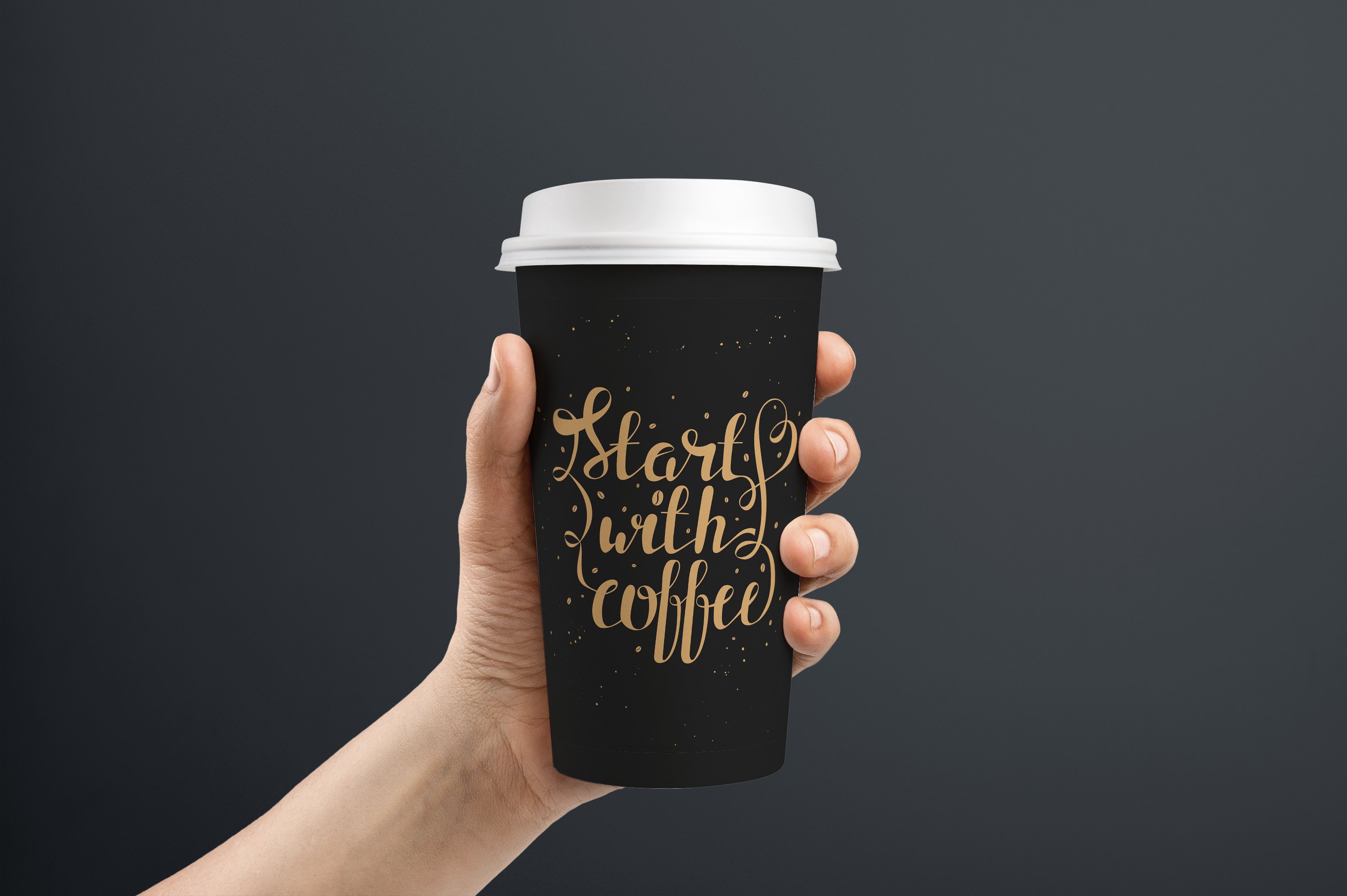 A hand holding a black coffee cup with gold lettering.