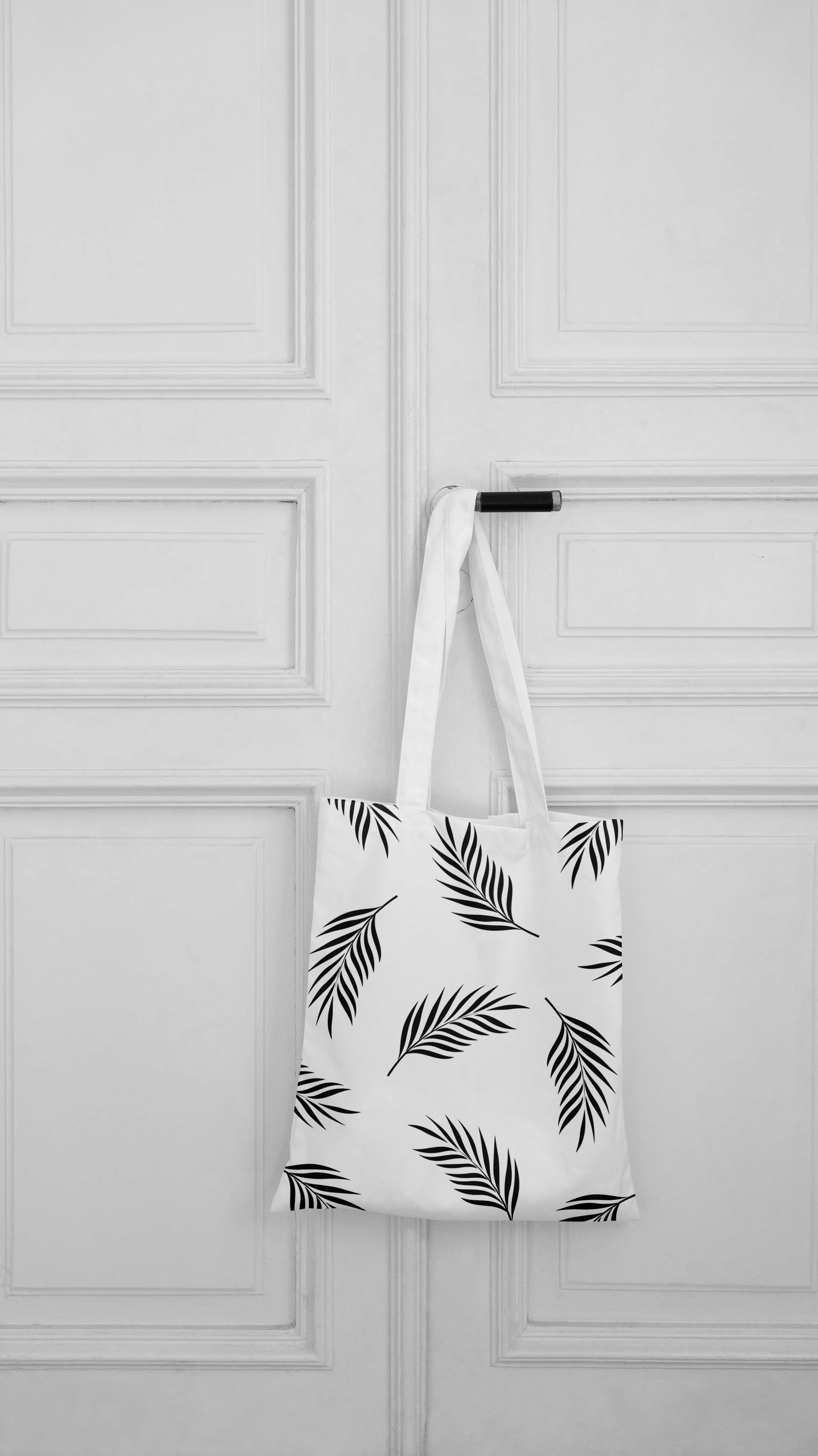 Black and white photo of a tote bag hanging on a door.