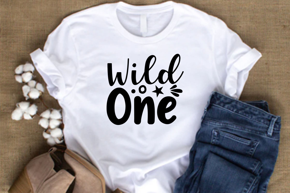 T - shirt that says wild is one next to a pair of jeans and.