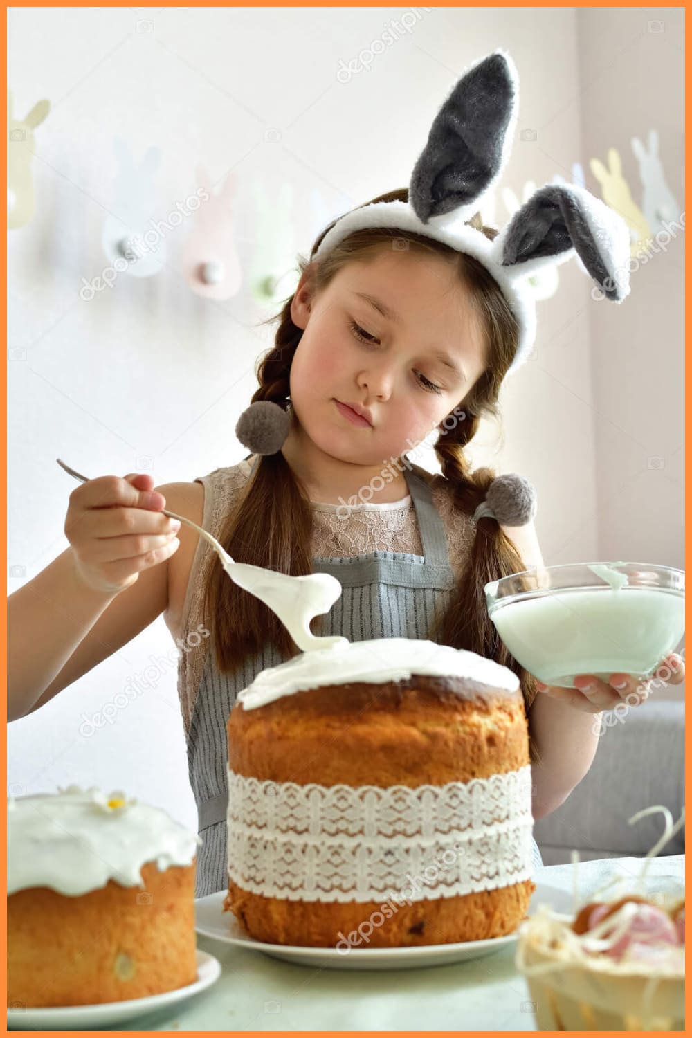 Smiling Girl with bunny ears covers easter cake with icing.Preparation to easter.Easter cake with green grass. Homemade pasques.Easter sweets on white background.