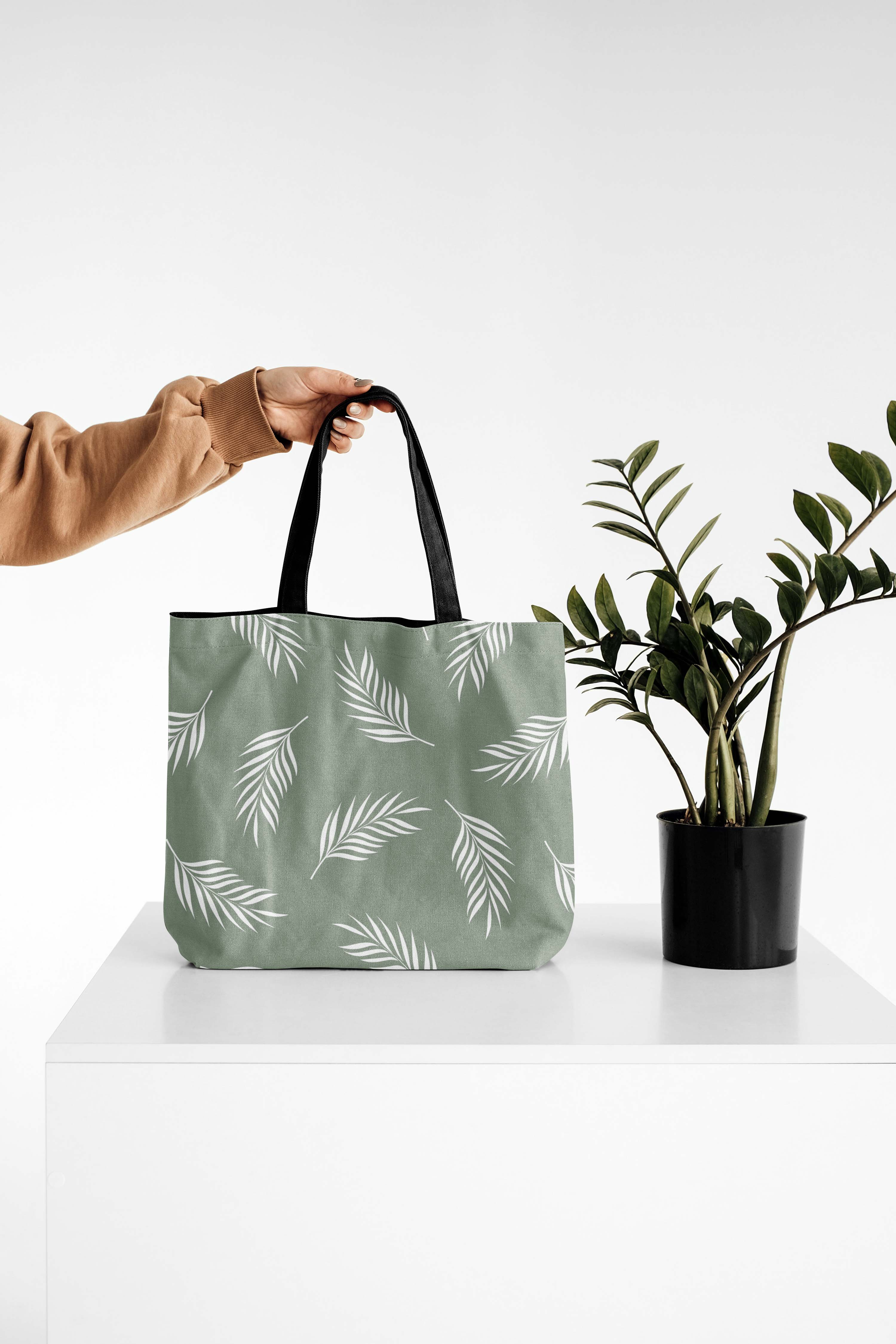 Person holding a green bag next to a plant.