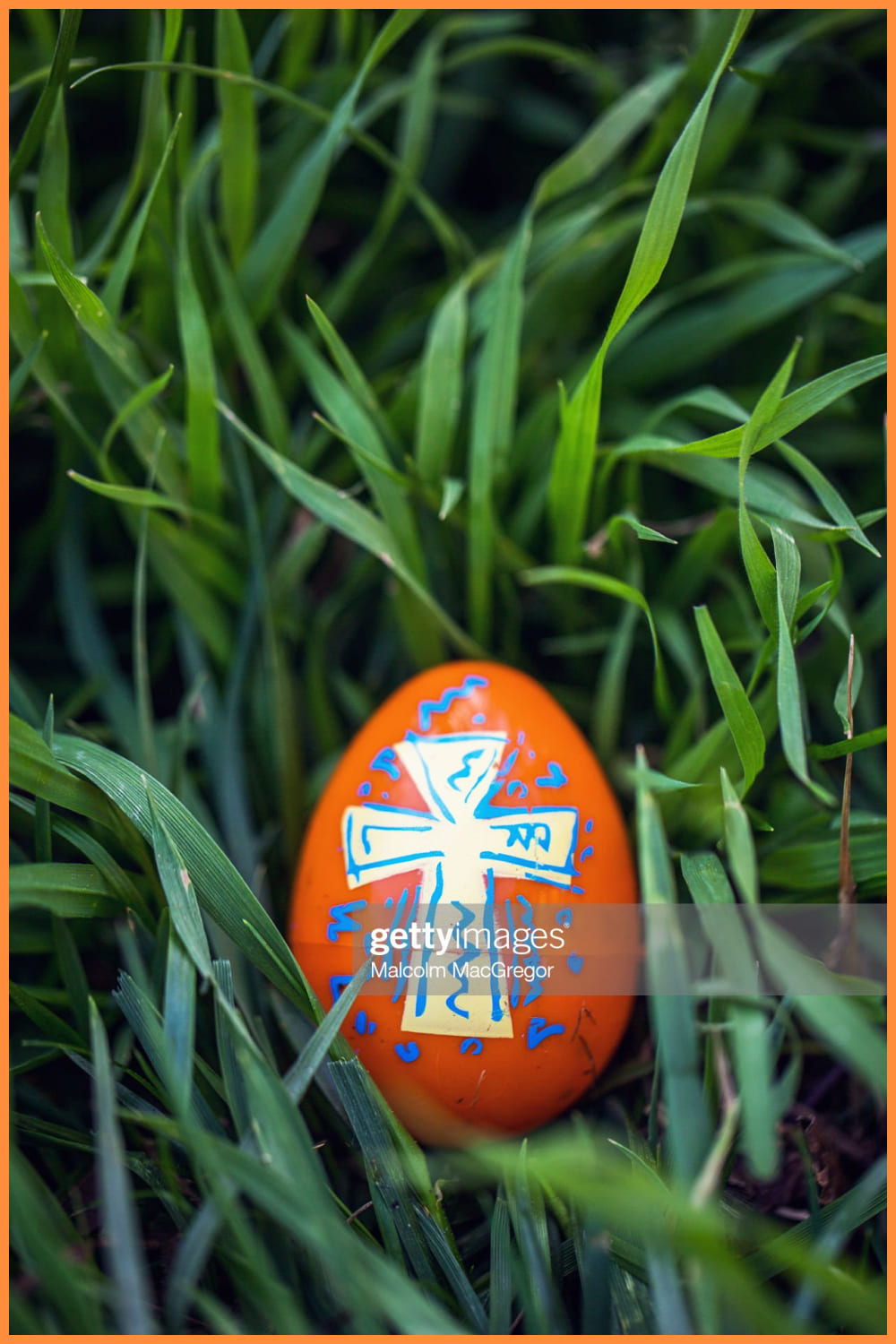 Easter egg with painted on cross design sits in tall green grass waiting to be found.