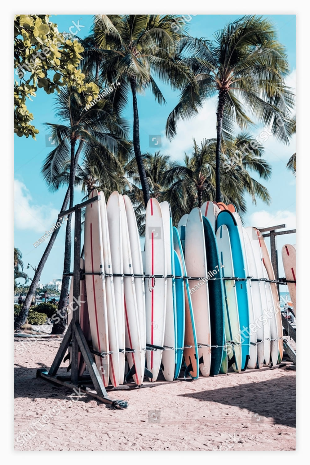 Surfboards in the rack on sandy beach with palm trees and ocean at famous Waikiki Beach in Honolulu, Hawaii.