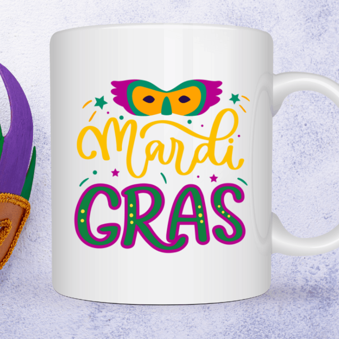 White coffee mug with mardi gras on it next to a pair of.