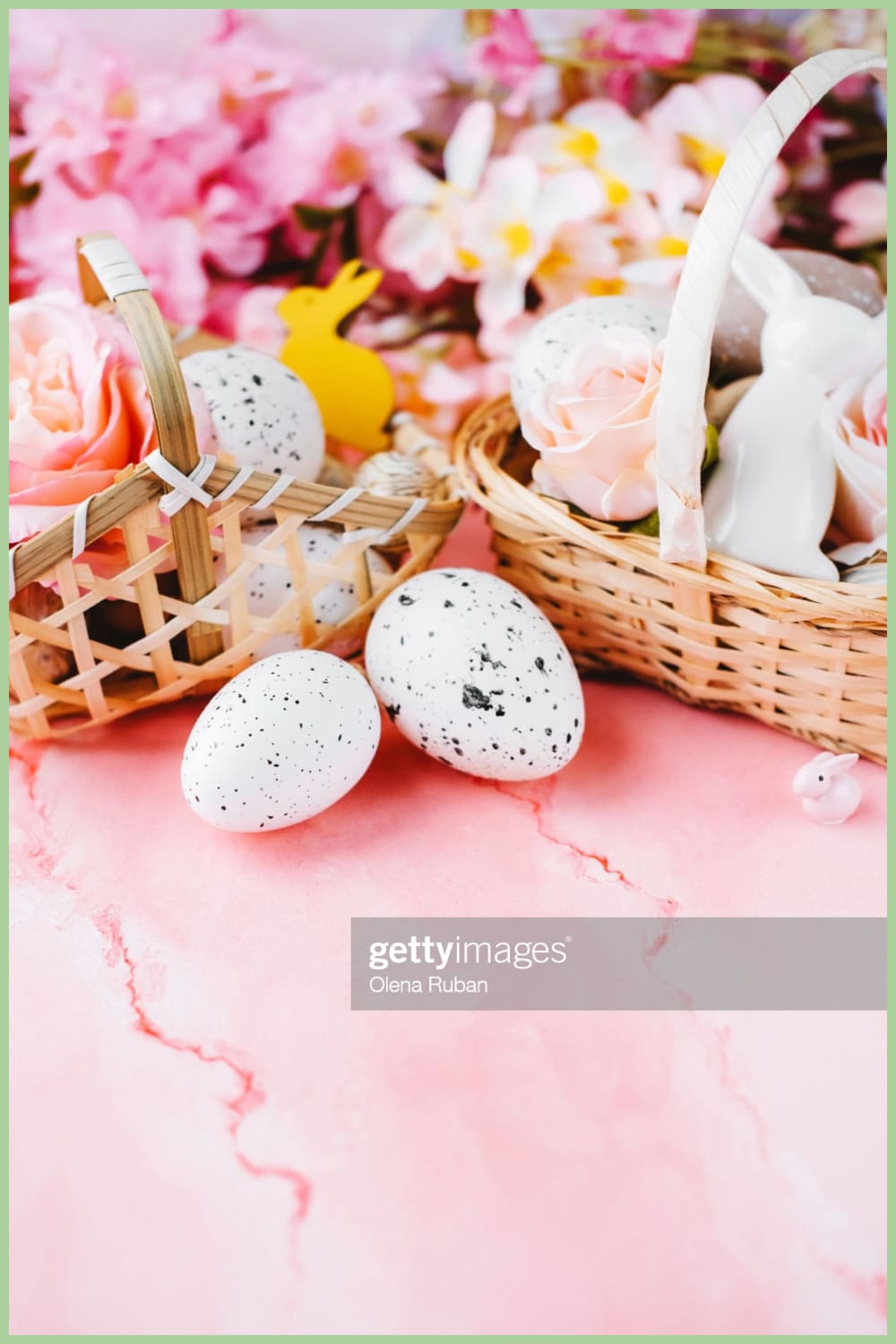 Quail eggs near wicker baskets with Easter stuff against blurred flowers on pink background.