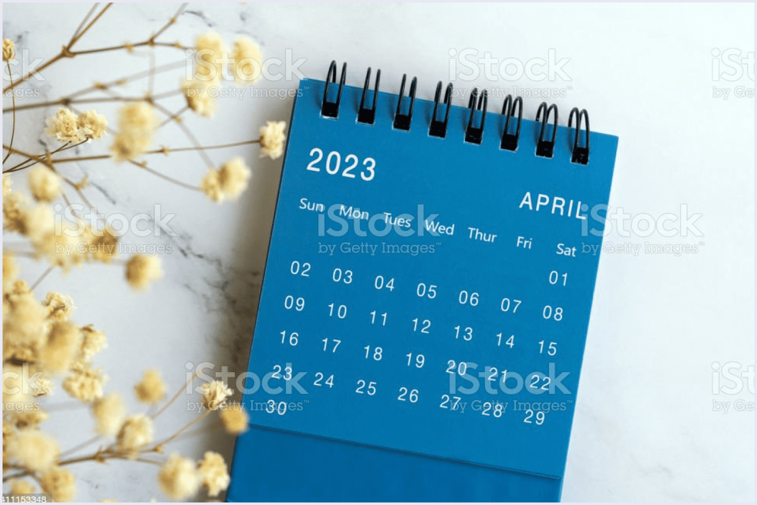 Photo of the calendar for April 2023 on a blue background and a twig of flowers.