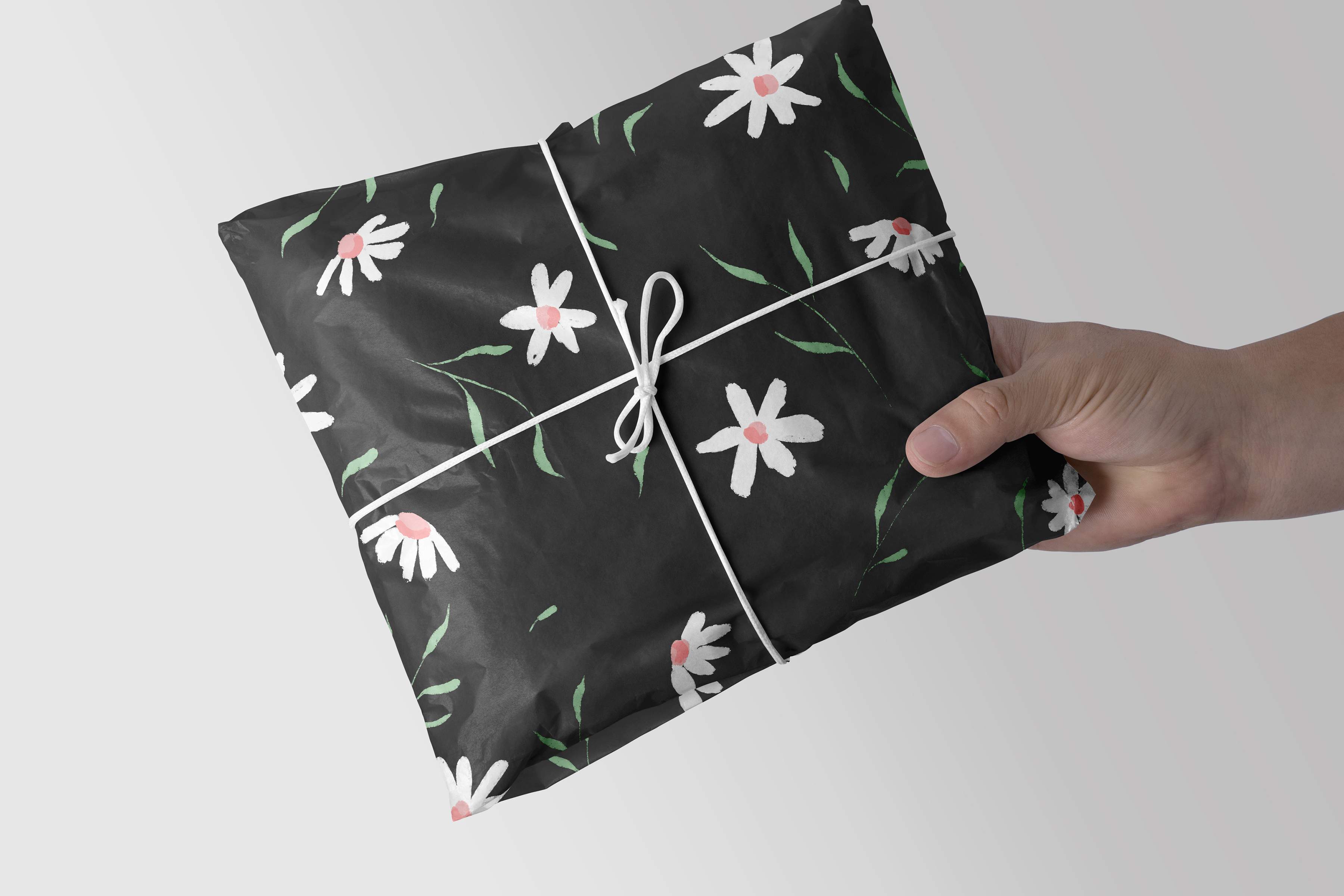 Hand is holding a black wrapping paper with white and pink flowers on it.