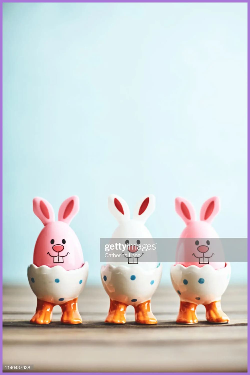 Easter bunny trio in eggcups with blue background and rustic table top.