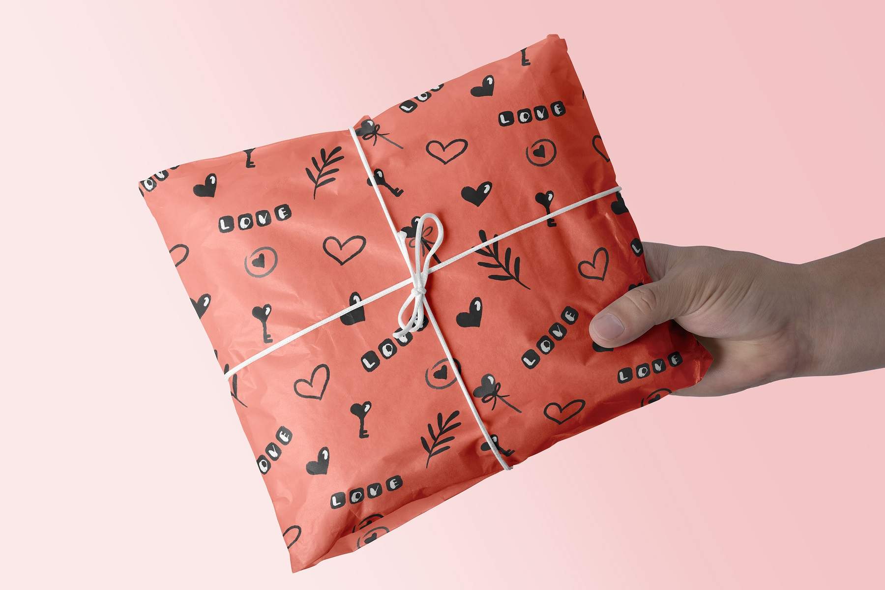 Hand holding a wrapped present on a pink background.