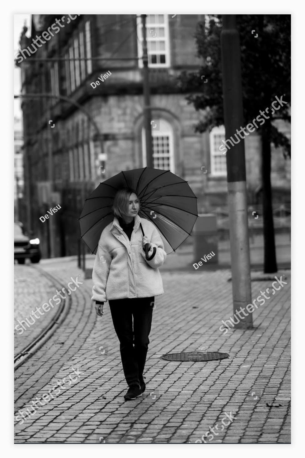 A woman with an umbrella stands on the street.