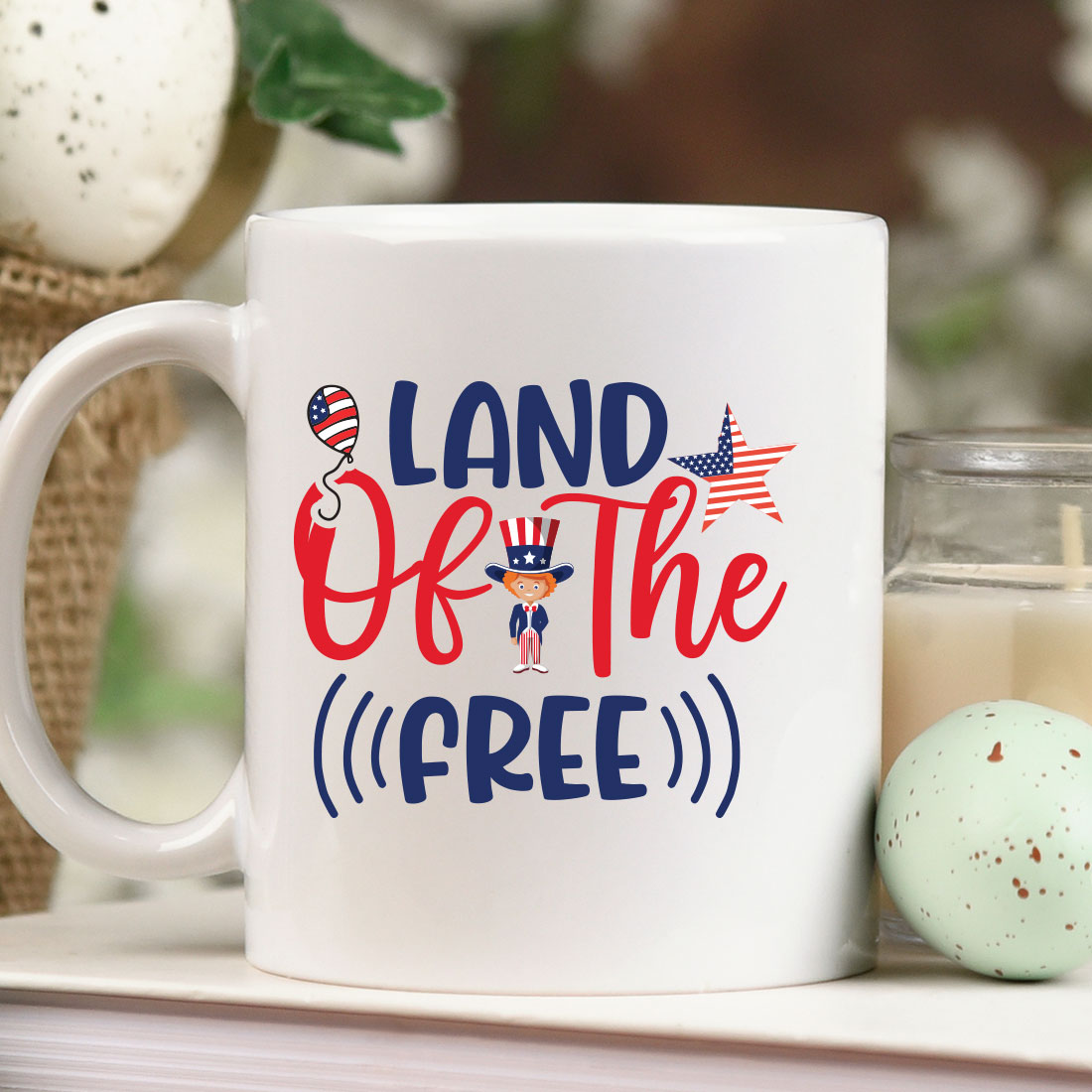 Coffee mug with the words land of the free on it next to a candle.