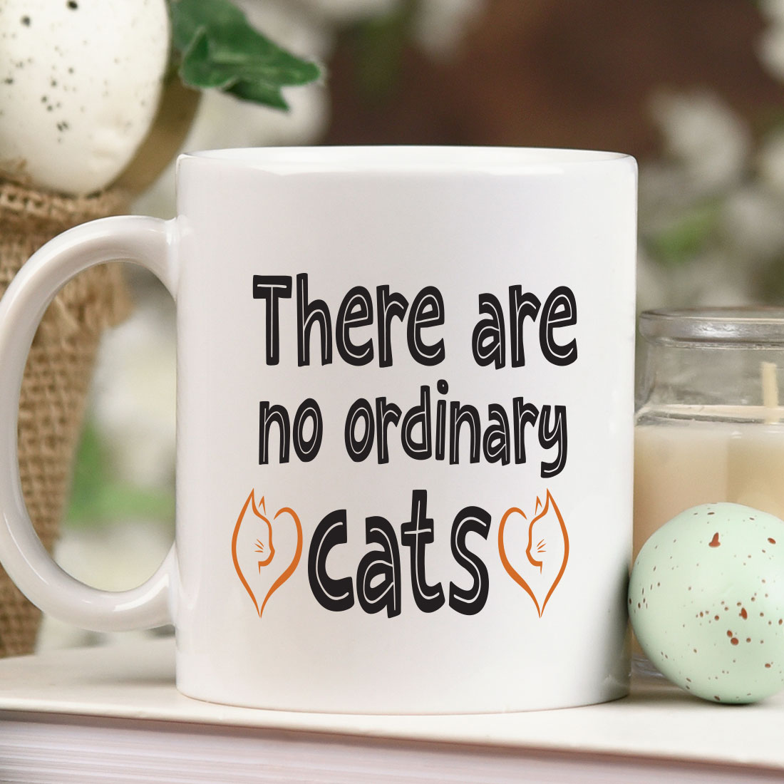 There are no ordinary cats mug next to a candle.