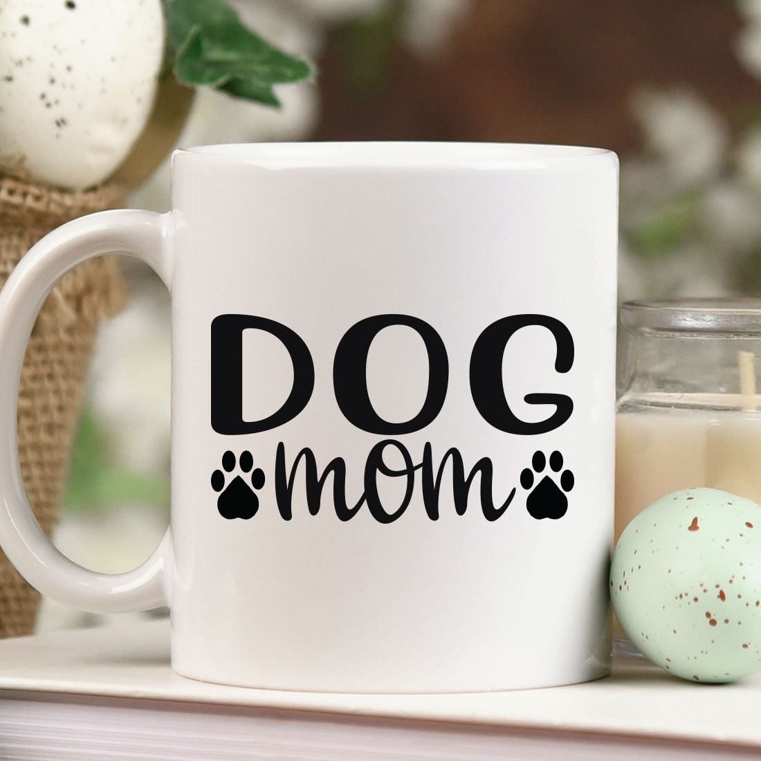 Coffee mug that says dog mom next to a candle.