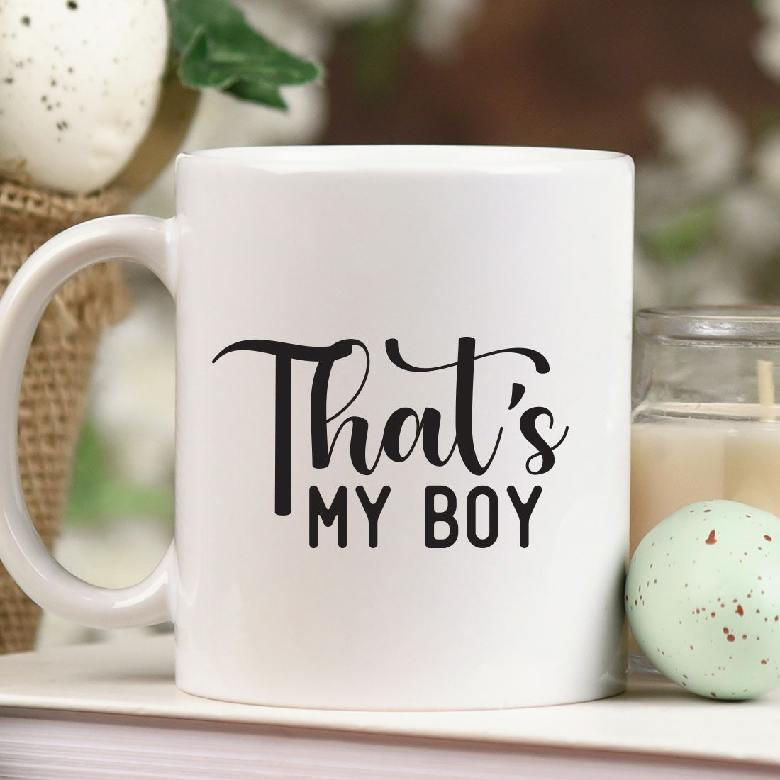 Coffee mug that says that's my boy next to a candle.