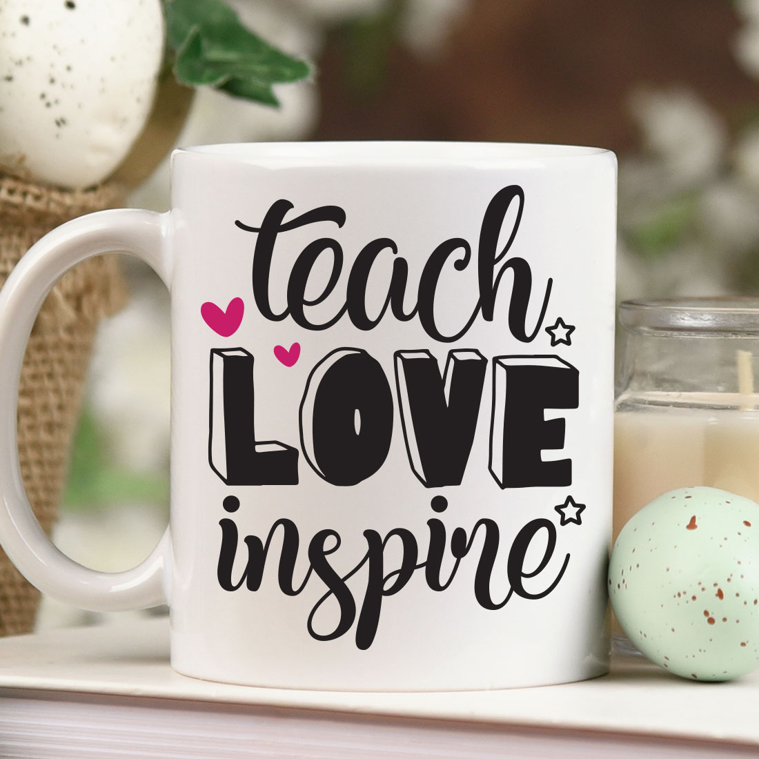 Coffee mug that says teach love inspire next to a candle.