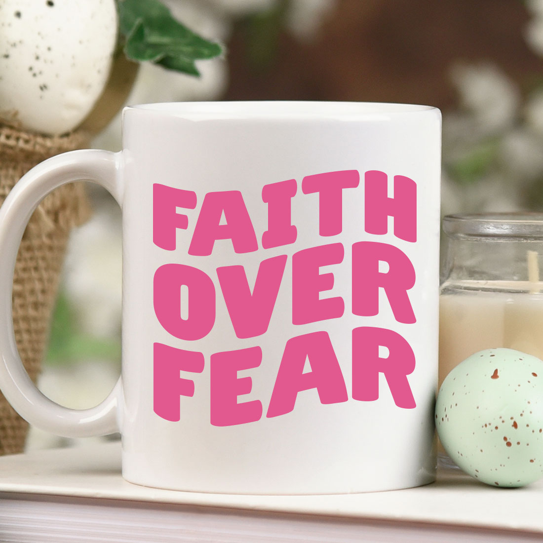 Coffee mug with the words faith over fear next to a candle.