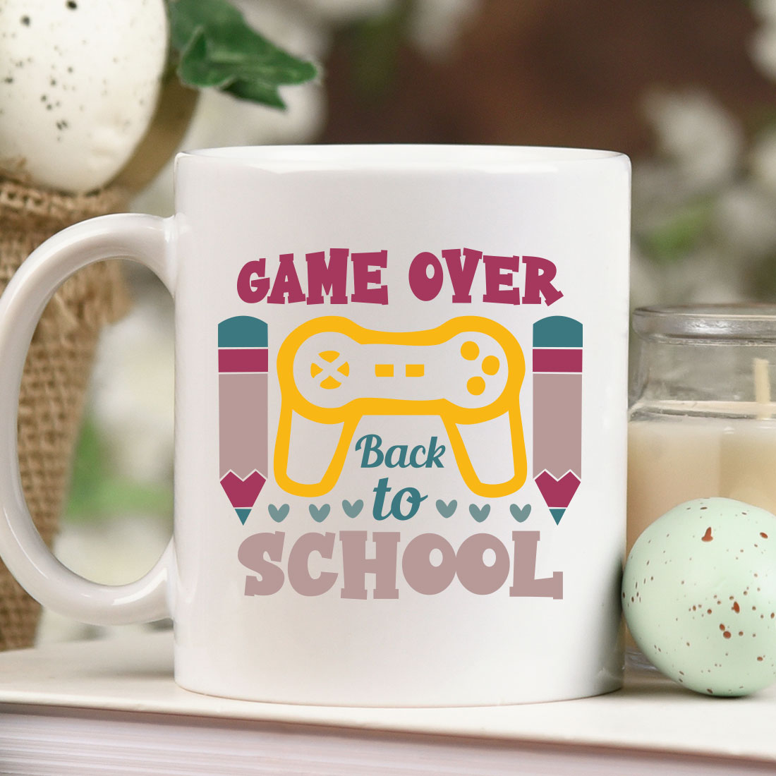 Coffee mug that says game over back to school next to a candle.