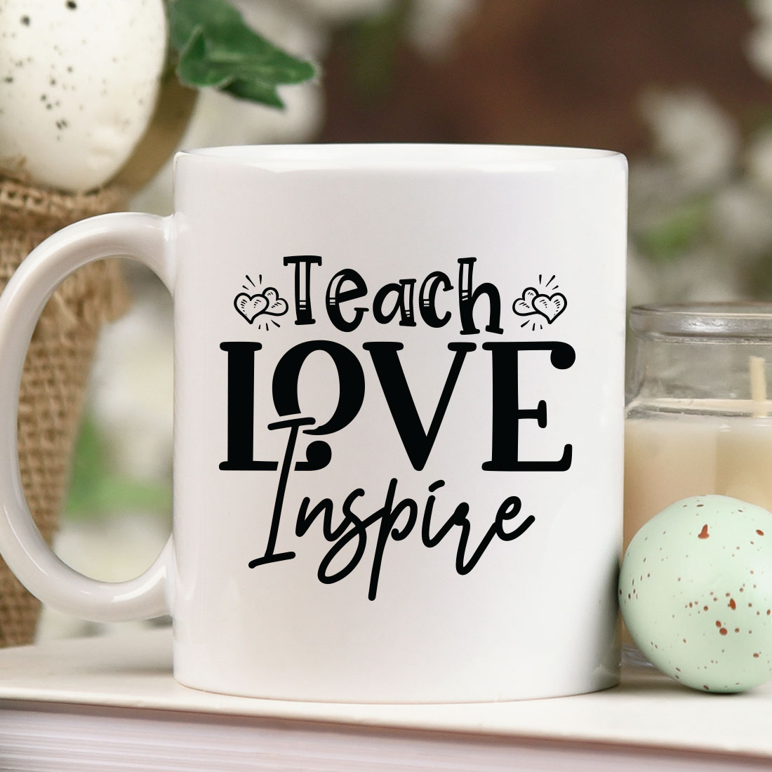 Coffee mug that says teach love inspire next to a candle.