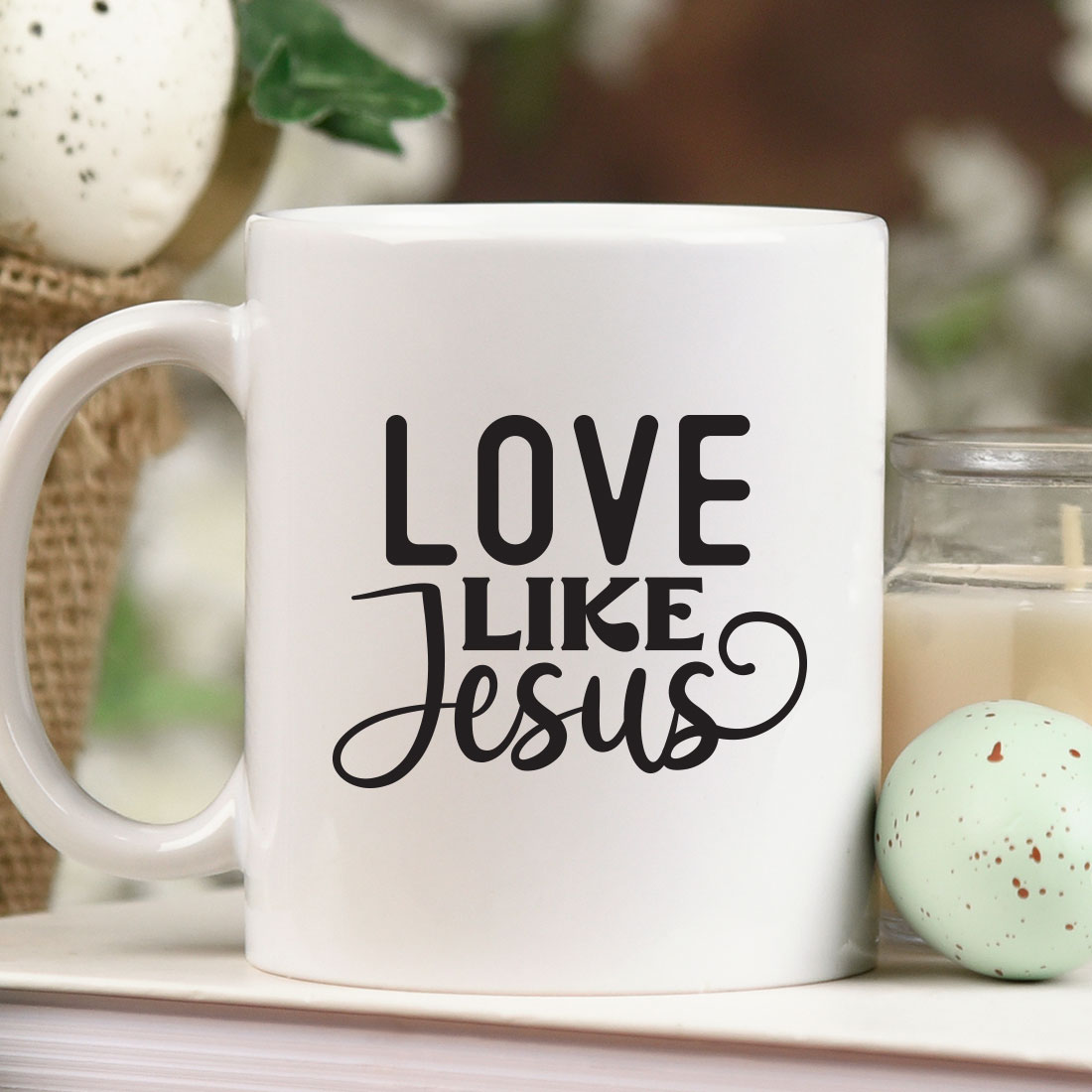 Coffee mug that says love like jesus next to a candle.