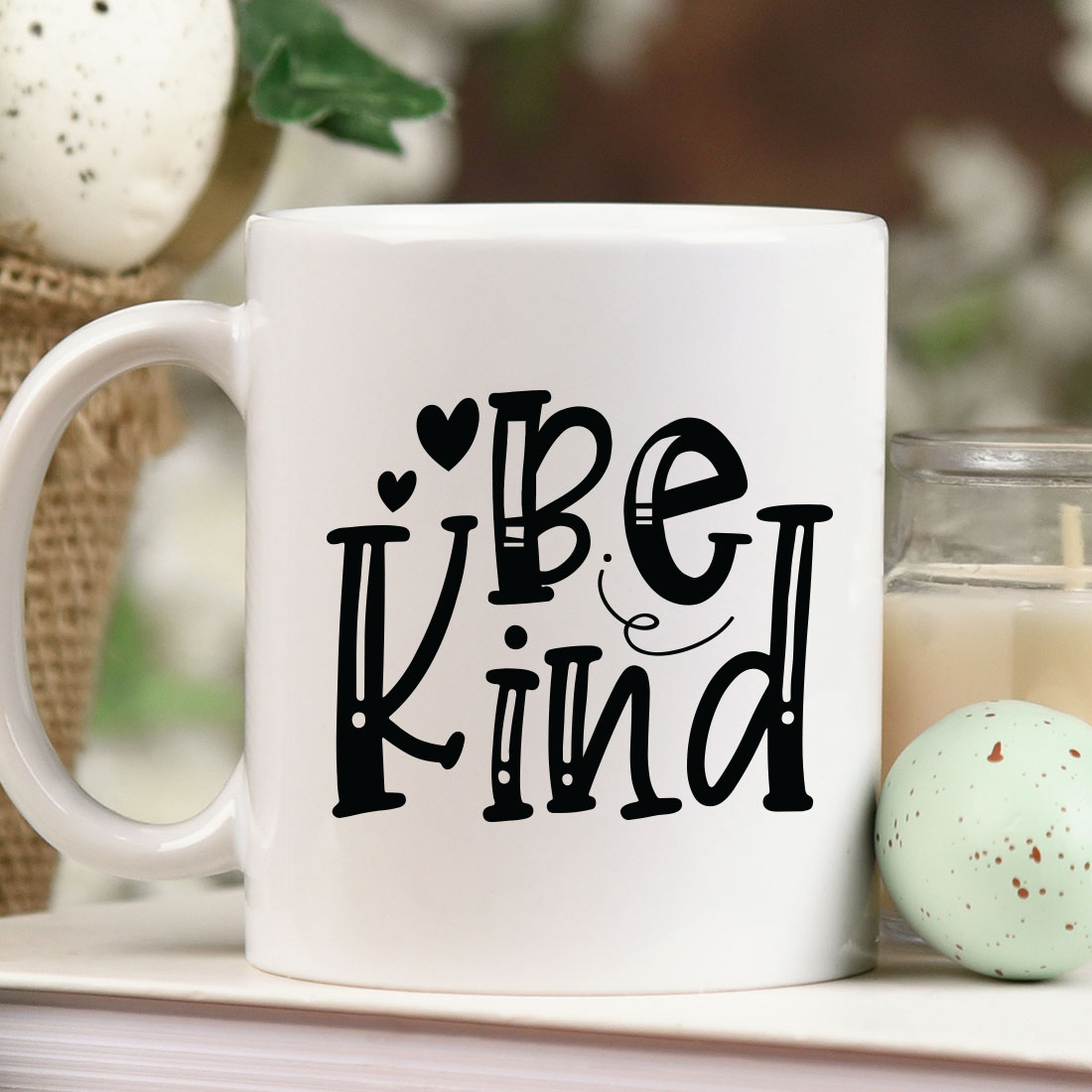 Coffee mug that says be kind next to a candle.