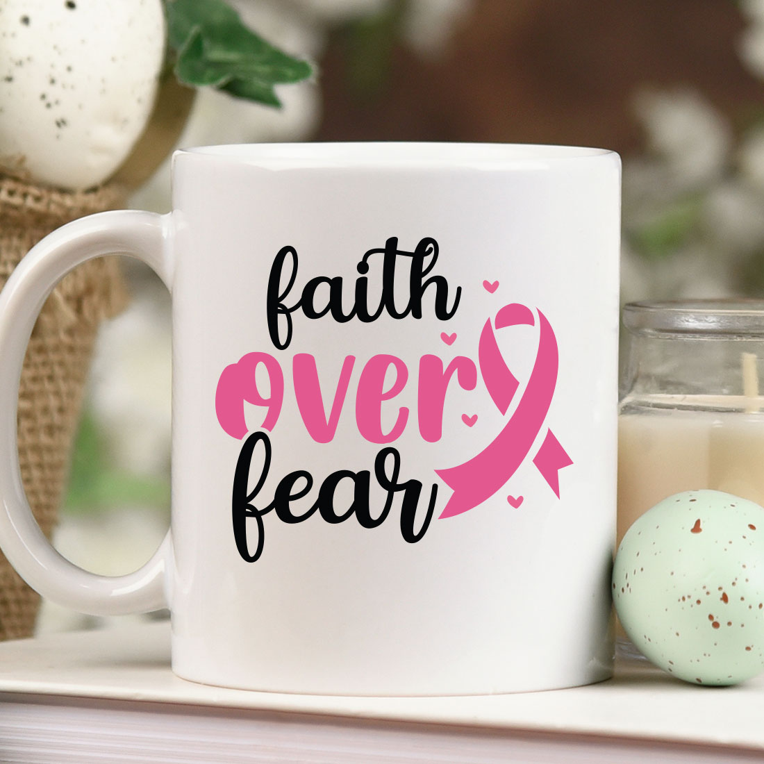 Coffee mug with a pink ribbon on it next to a candle.