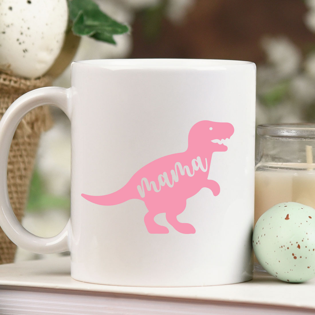 Pink dinosaur mug sitting on top of a table next to a candle.