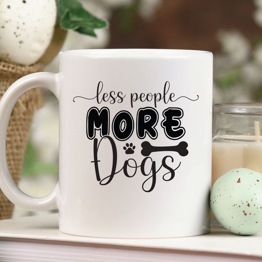 Coffee mug that says less people more dogs next to a candle.