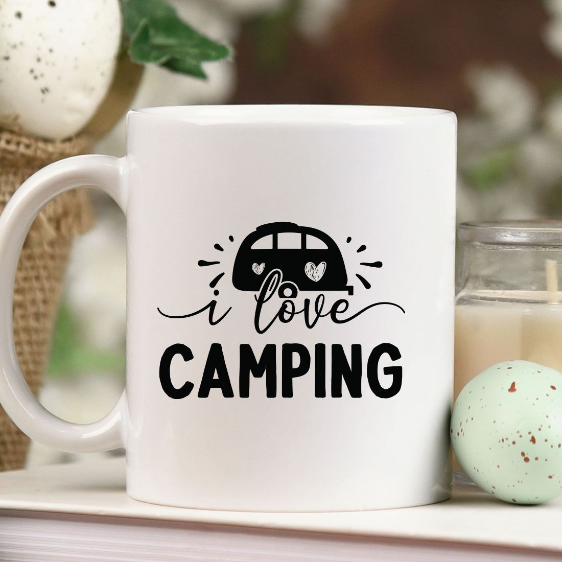Coffee mug that says i love camping next to a candle.