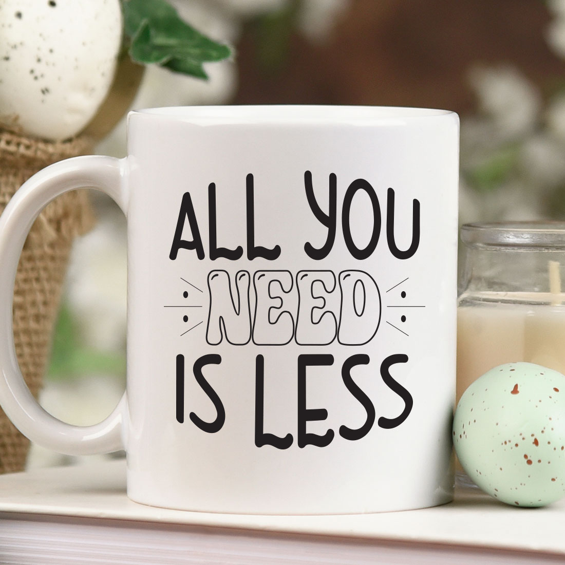 Coffee mug that says all you need is less next to a candle.