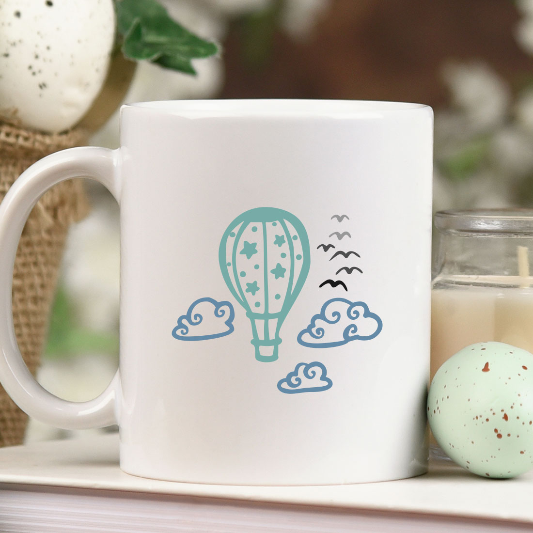 Mug with a hot air balloon on it next to a candle.