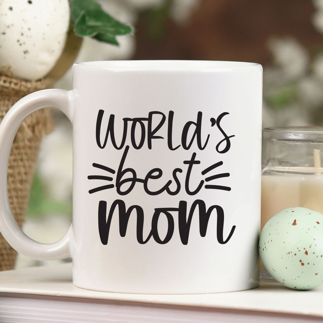 Coffee mug that says world's best mom next to a candle.