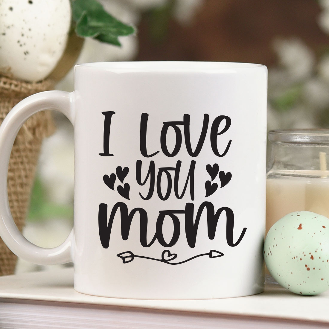 Coffee mug that says i love you mom next to a candle.