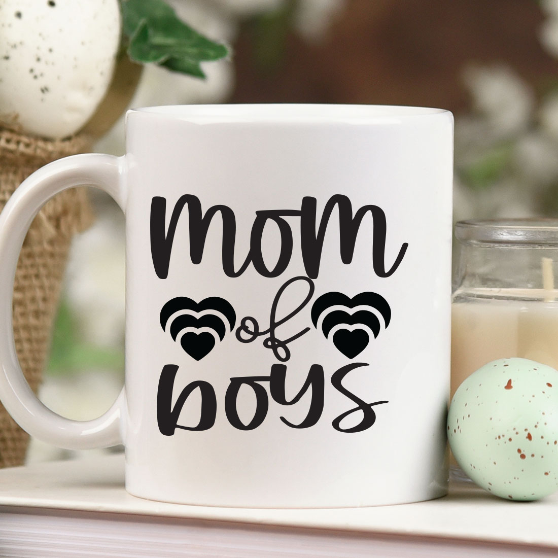 Coffee mug that says mom of boys next to a candle.