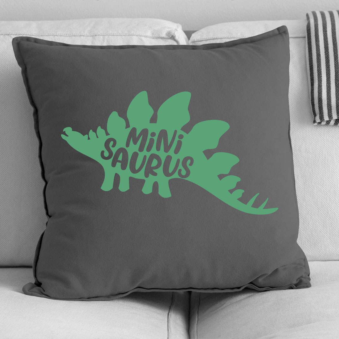 Black and white photo of a pillow with a green dinosaur on it.