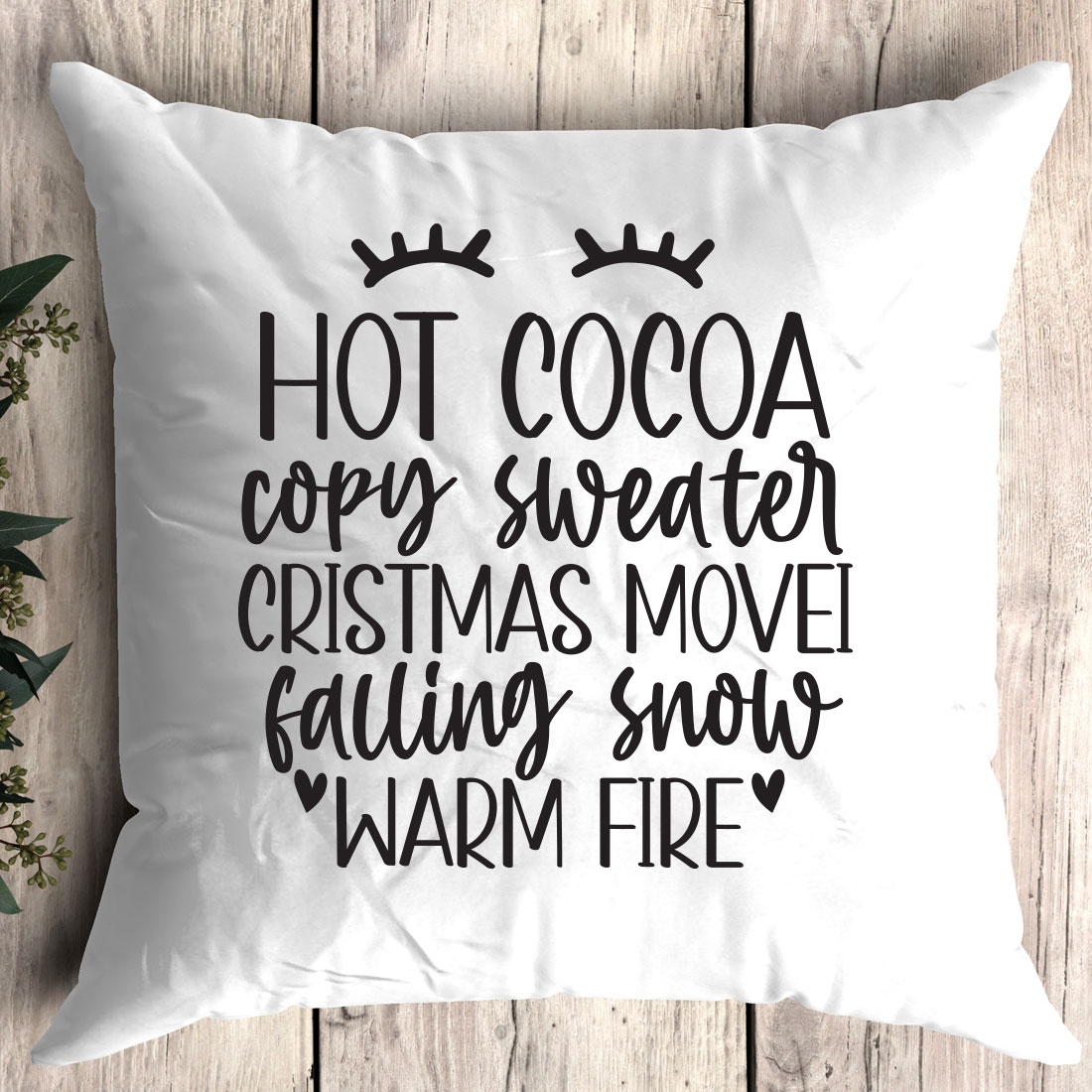 White pillow with the words hot cocoa cozy sweater christmas movie falling snow warm fire.