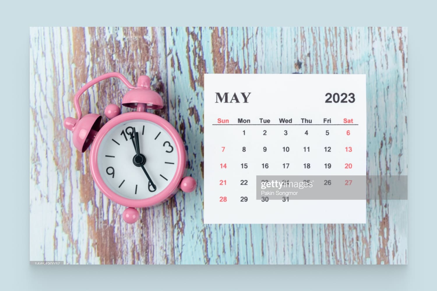 Calendar for May 2023 with an alarm clock on a wooden table background.